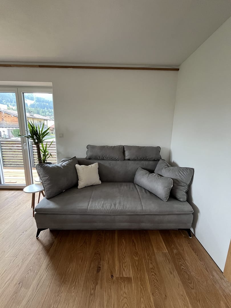 Home Helles Wohnzimmer mit grauem Sofa und Zugang zum Balkon in den AlpineHome Walchsee Apartments