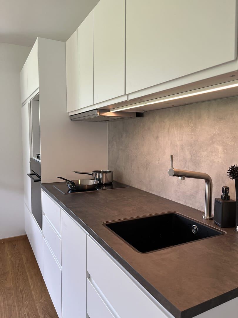 Home Küchenzeile mit dunkler Arbeitsplatte, Spüle und Kochfeld in den AlpineHome Walchsee Apartments